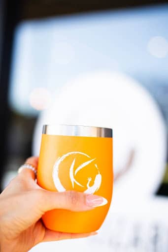 A woman’s hand holding a cup of freshly brewed Kinky Lizard coffee in the official orange-colored Kinky Lizard coffee mug.