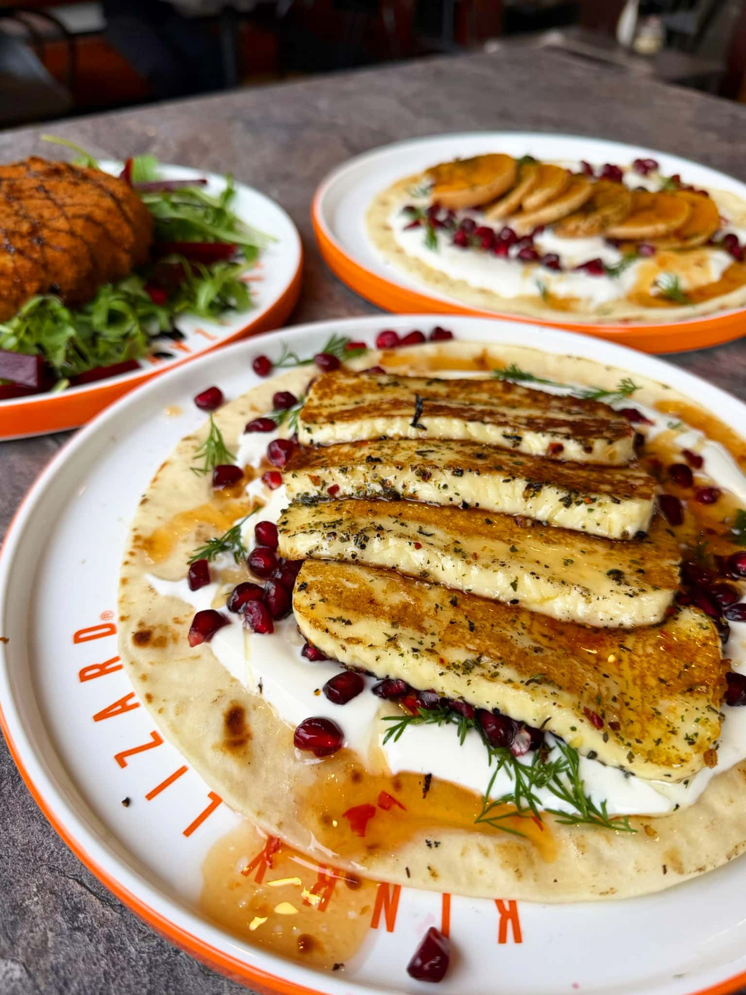 Seafood dish with pan-seared fish fillets arranged on creamy sauce, sprinkled with pomegranate seeds and dill, on a white plate with an orange rim.