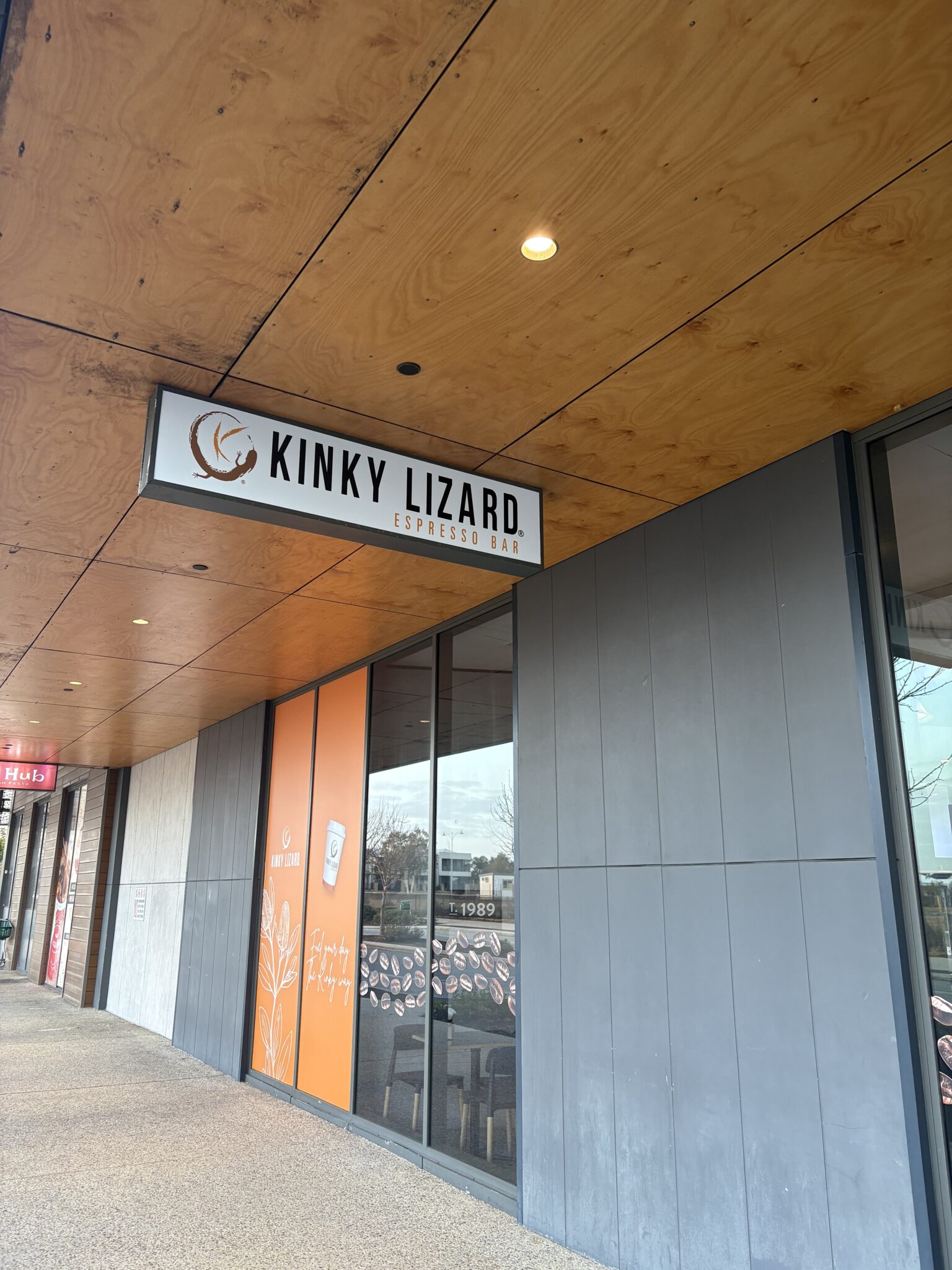 Storefront with a sign reading 'Kinky Lizard Espresso Bar' under a wood-paneled awning and large orange panels on the windows exterior.