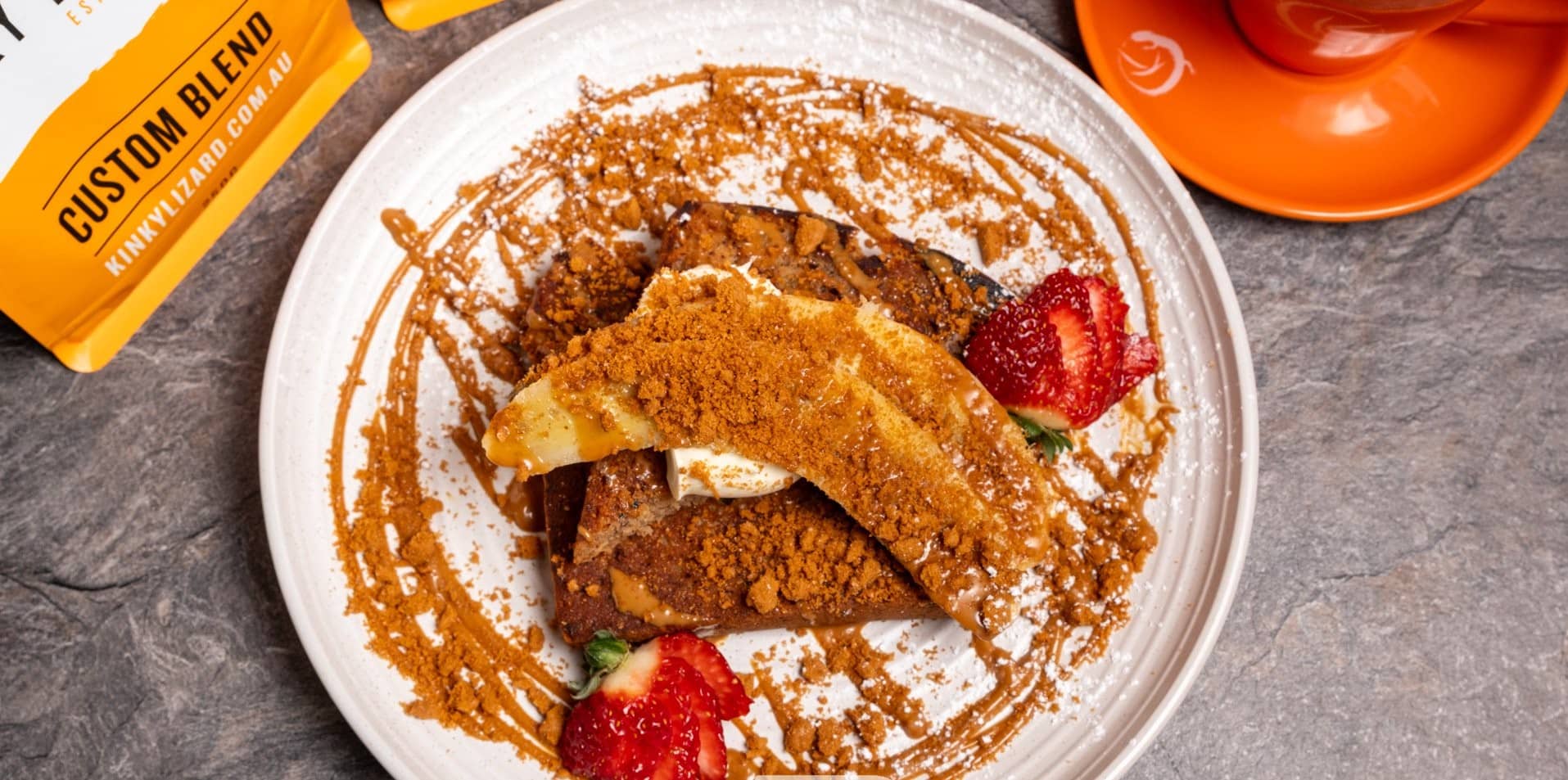 Dessert plate with cinnamon crumble, strawberry halves, and caramel drizzle on a gray table surface.