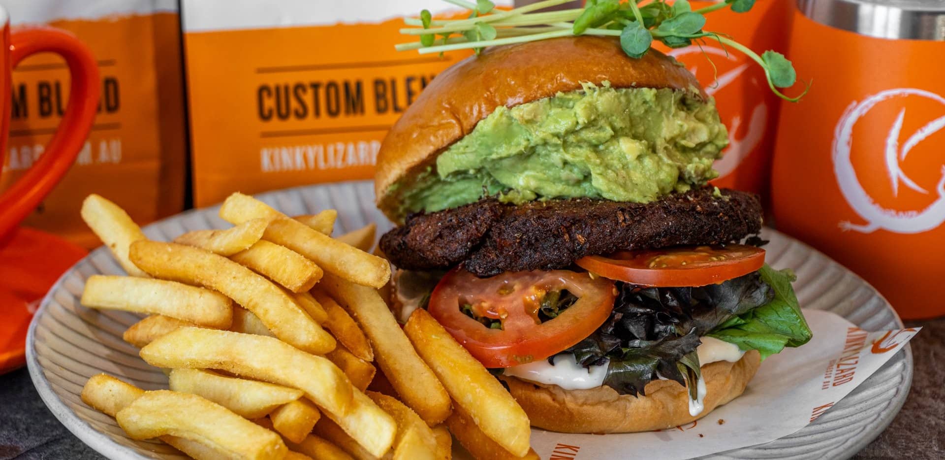 Burger with avocado spread, tomato and lettuce on a bun, served with golden fries on a plate.